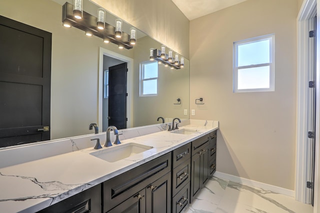 full bath featuring marble finish floor, a sink, baseboards, and double vanity