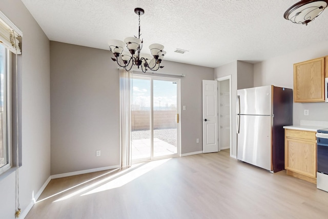 kitchen with light brown cabinets, light countertops, light wood-style flooring, freestanding refrigerator, and a notable chandelier