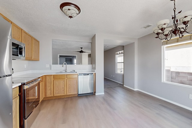 kitchen with a sink, a textured ceiling, appliances with stainless steel finishes, light wood finished floors, and light countertops