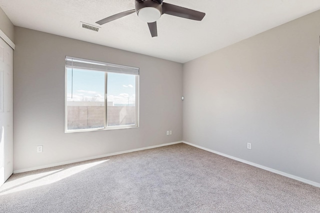 carpeted spare room featuring baseboards, visible vents, and ceiling fan