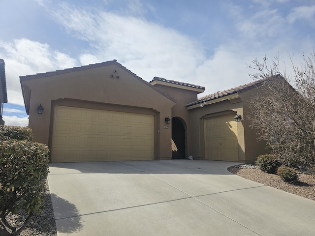 mediterranean / spanish home featuring concrete driveway, a tiled roof, an attached garage, and stucco siding