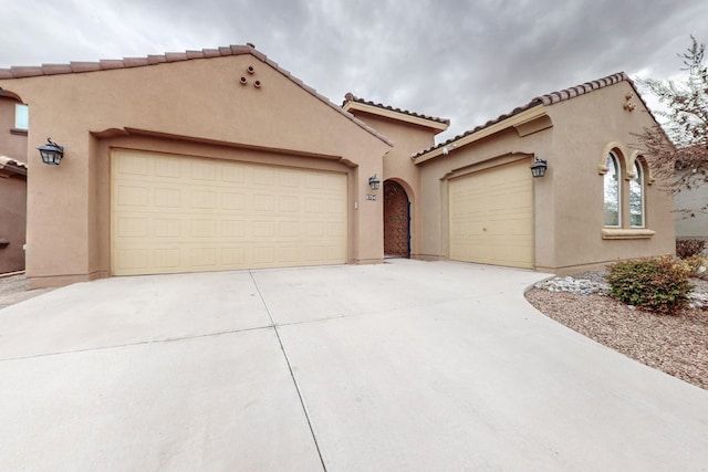 mediterranean / spanish-style home featuring a tiled roof, a garage, driveway, and stucco siding