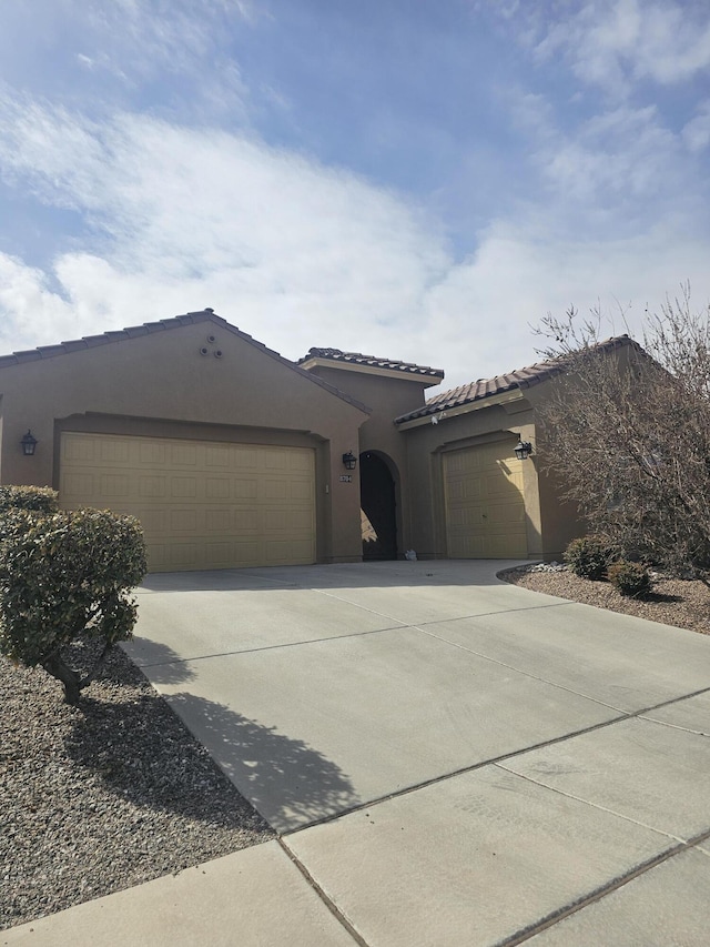 mediterranean / spanish house featuring driveway, a tiled roof, an attached garage, and stucco siding