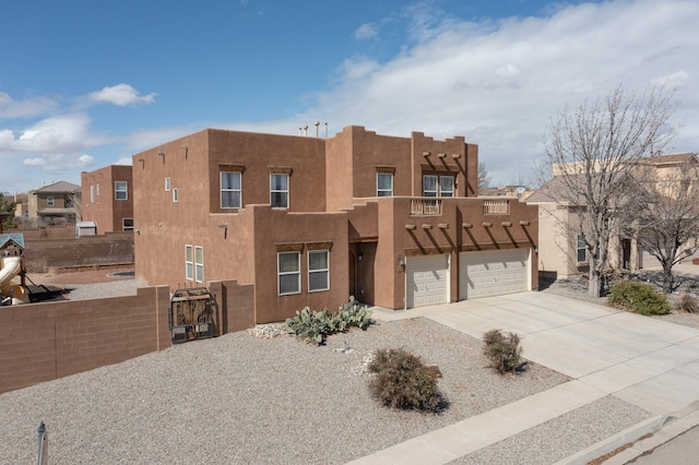 adobe home featuring fence, concrete driveway, and stucco siding