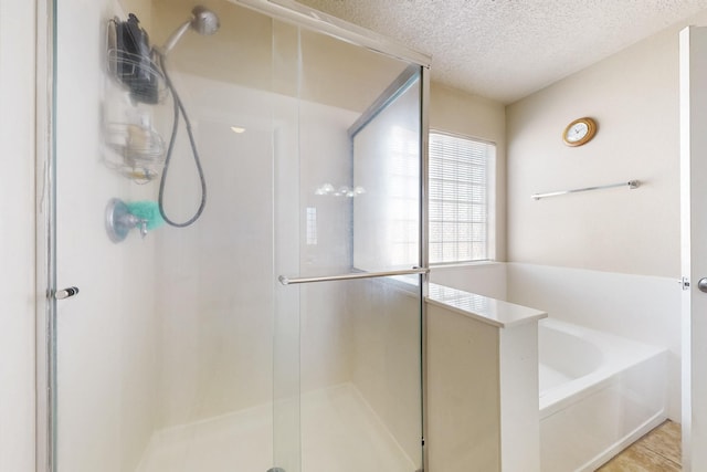 full bathroom featuring a bath, a stall shower, and a textured ceiling