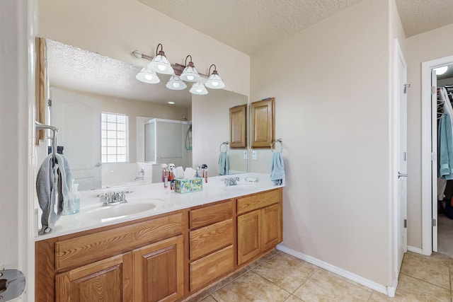 bathroom with double vanity, a textured ceiling, a stall shower, and a sink