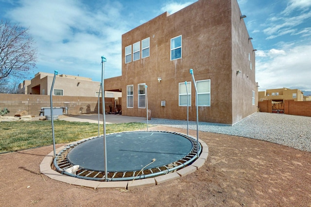 rear view of house featuring a patio, a trampoline, a fenced backyard, and stucco siding