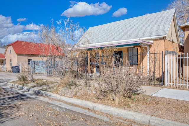 view of front of home with roof with shingles, fence, and stucco siding