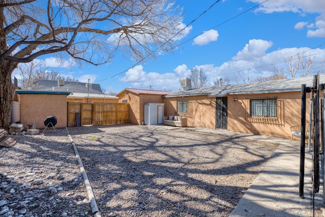 rear view of property with stucco siding, a gate, central AC, fence, and an outdoor structure