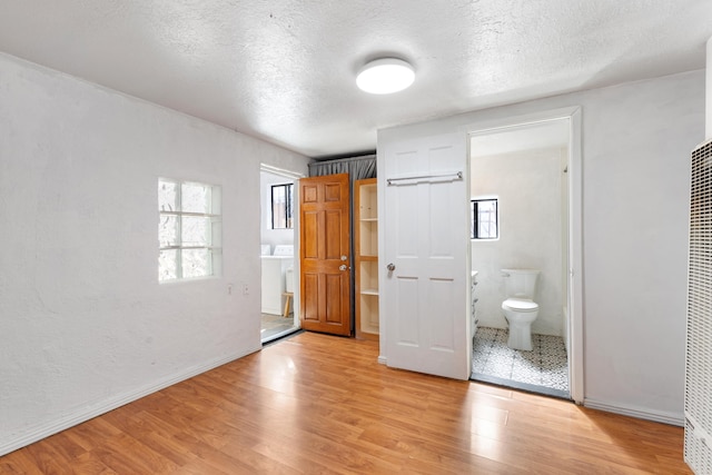 unfurnished bedroom featuring light wood-type flooring, baseboards, a textured ceiling, and ensuite bathroom