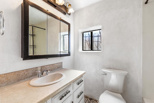 bathroom with a textured wall, vanity, and toilet