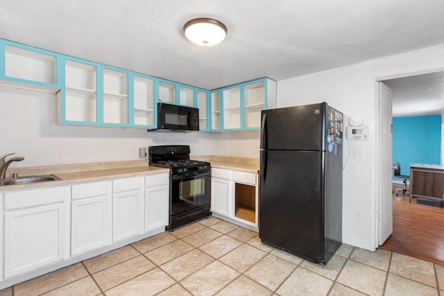 kitchen with white cabinets, light countertops, black appliances, open shelves, and a sink