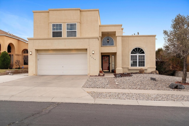 pueblo-style house featuring a garage, concrete driveway, and stucco siding