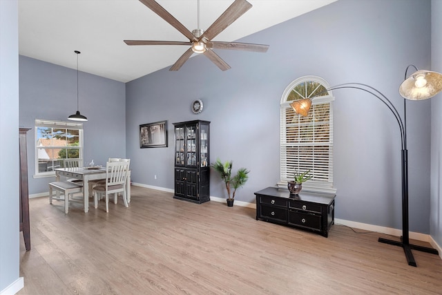 dining area featuring a ceiling fan, a towering ceiling, light wood-style flooring, and baseboards