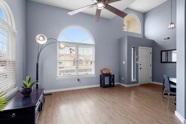 entryway with visible vents, baseboards, a ceiling fan, a towering ceiling, and light wood-style flooring