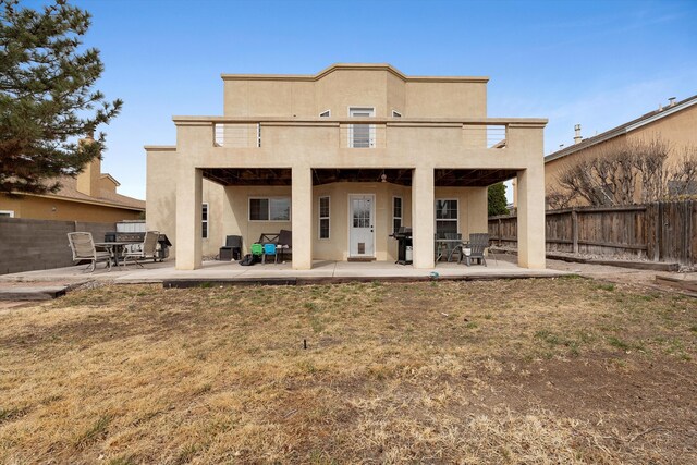 rear view of house with a patio, a fenced backyard, a balcony, a yard, and stucco siding