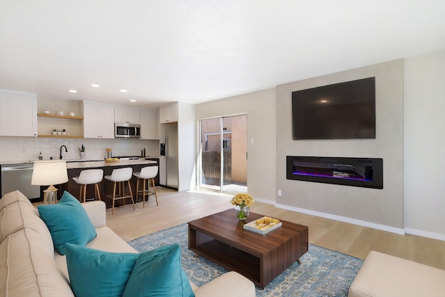 living area featuring light wood-type flooring, a glass covered fireplace, baseboards, and recessed lighting