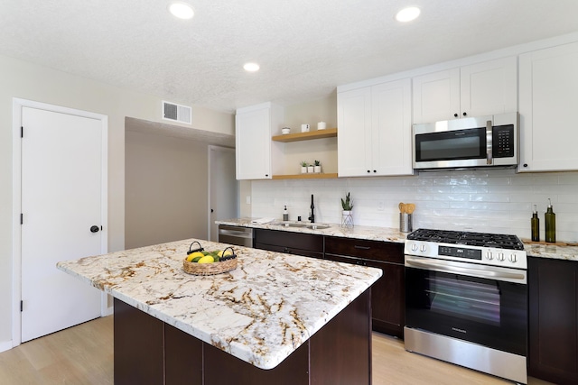 kitchen featuring open shelves, appliances with stainless steel finishes, a sink, and light wood-style floors