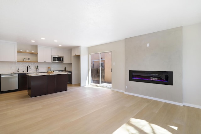 kitchen featuring stainless steel appliances, backsplash, light wood-style flooring, a glass covered fireplace, and white cabinets