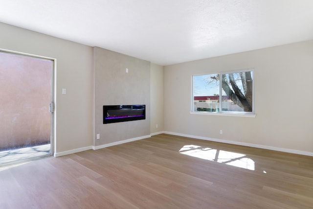 unfurnished living room with baseboards, wood finished floors, and a glass covered fireplace