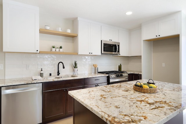 kitchen with white cabinets, light stone counters, stainless steel appliances, and a sink