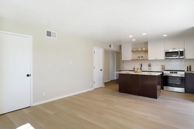 kitchen featuring light wood finished floors, visible vents, baseboards, appliances with stainless steel finishes, and backsplash