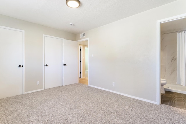 unfurnished bedroom with ensuite bathroom, a textured ceiling, visible vents, baseboards, and carpet