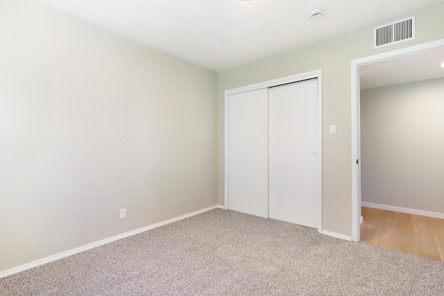 unfurnished bedroom with a closet, visible vents, light carpet, and baseboards