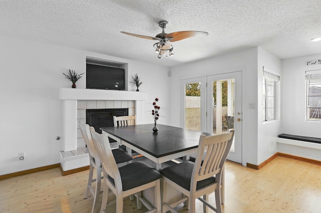 dining area featuring baseboards, light wood-type flooring, a tiled fireplace, and ceiling fan