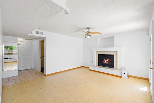 unfurnished living room featuring visible vents, a textured ceiling, wood finished floors, ceiling fan, and a tile fireplace