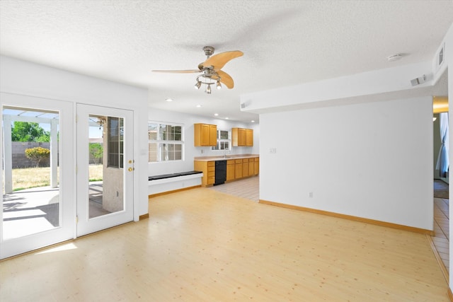 unfurnished living room featuring a wealth of natural light, a textured ceiling, light wood-type flooring, and baseboards