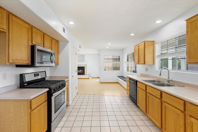 kitchen featuring visible vents, a lit fireplace, a sink, light countertops, and appliances with stainless steel finishes