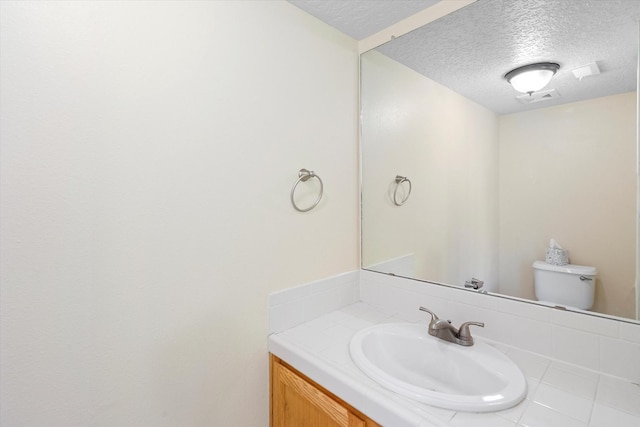 half bathroom featuring vanity, toilet, visible vents, and a textured ceiling