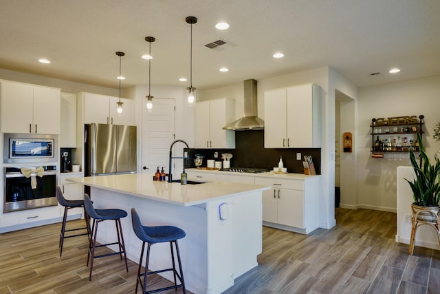 kitchen featuring a breakfast bar area, a sink, appliances with stainless steel finishes, wall chimney exhaust hood, and tasteful backsplash