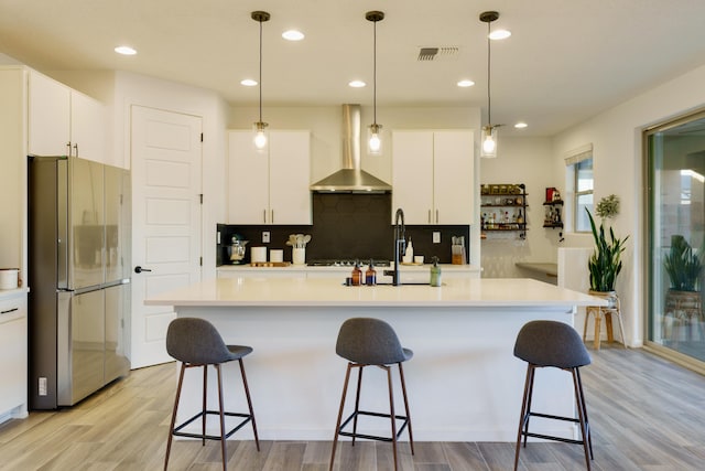 kitchen with wall chimney exhaust hood, visible vents, light countertops, and freestanding refrigerator