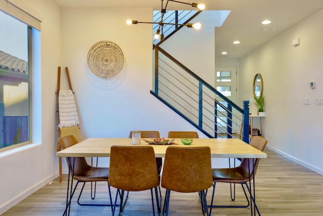 dining room with light wood-type flooring, an inviting chandelier, stairs, and baseboards