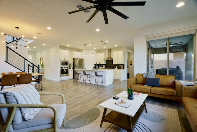 living room with light wood-style floors, recessed lighting, stairs, and ceiling fan with notable chandelier