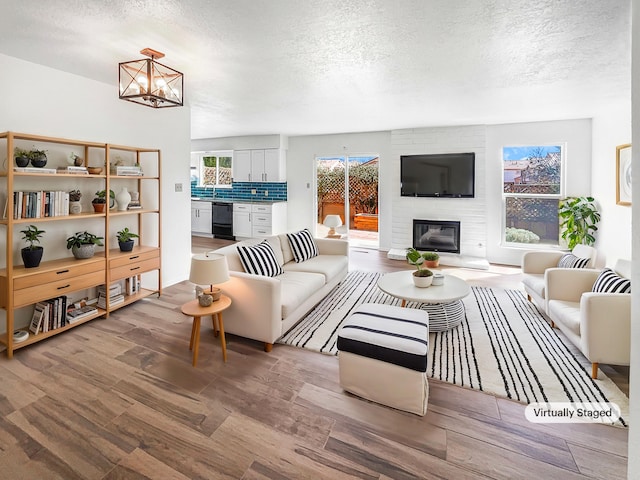 living area with an inviting chandelier, a brick fireplace, wood finished floors, and a textured ceiling