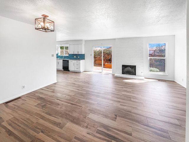 unfurnished living room with visible vents, a chandelier, a fireplace, wood finished floors, and a textured ceiling