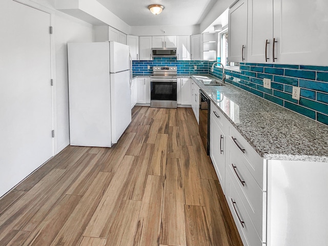 kitchen with electric range, a sink, black dishwasher, wood finished floors, and freestanding refrigerator