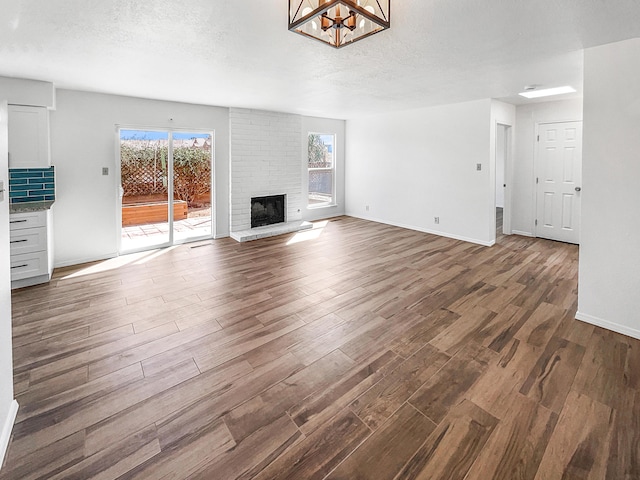 unfurnished living room with a wealth of natural light, dark wood finished floors, a brick fireplace, and a textured ceiling