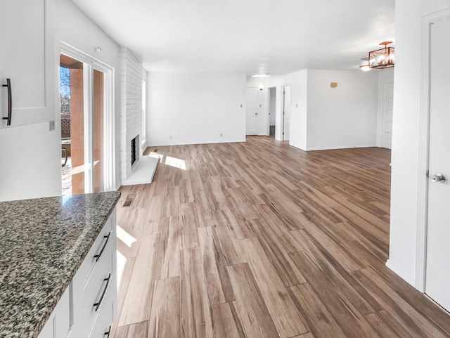 unfurnished living room with baseboards, a brick fireplace, light wood-style flooring, and an inviting chandelier