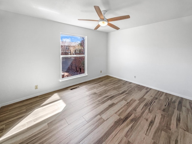 spare room with a ceiling fan, wood finished floors, visible vents, and baseboards