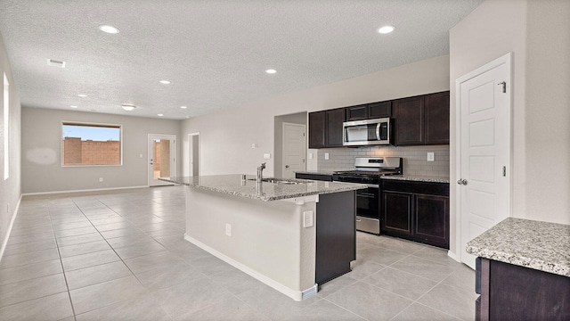 kitchen with light tile patterned floors, an island with sink, a sink, decorative backsplash, and stainless steel appliances