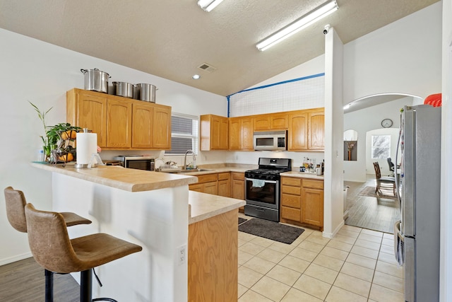 kitchen with visible vents, a breakfast bar area, appliances with stainless steel finishes, a peninsula, and a sink