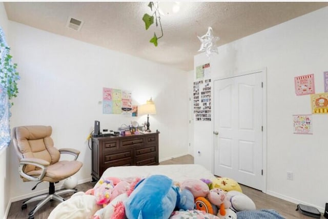 bedroom featuring visible vents, a textured ceiling, baseboards, and wood finished floors