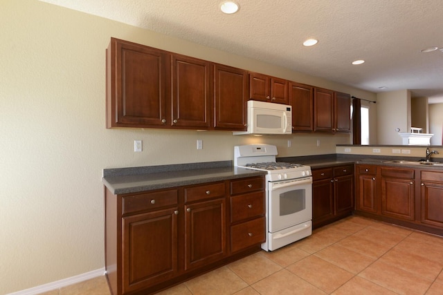 kitchen with dark countertops, light tile patterned floors, white appliances, and a sink