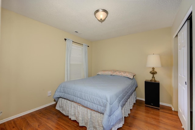 bedroom with visible vents, baseboards, a closet, and wood finished floors