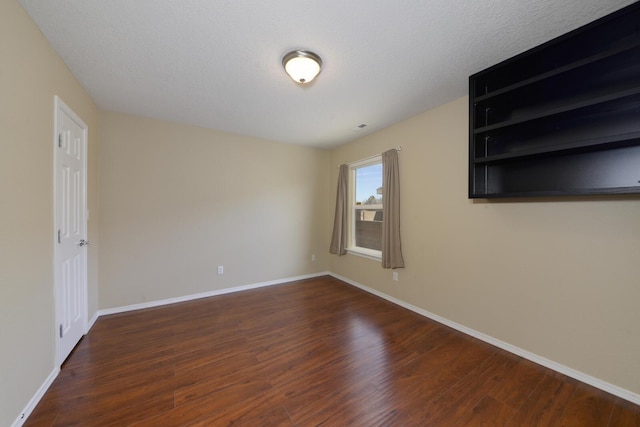 spare room with a textured ceiling, baseboards, and dark wood-style flooring