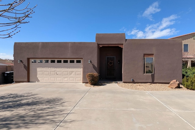 pueblo-style home featuring stucco siding, driveway, and an attached garage